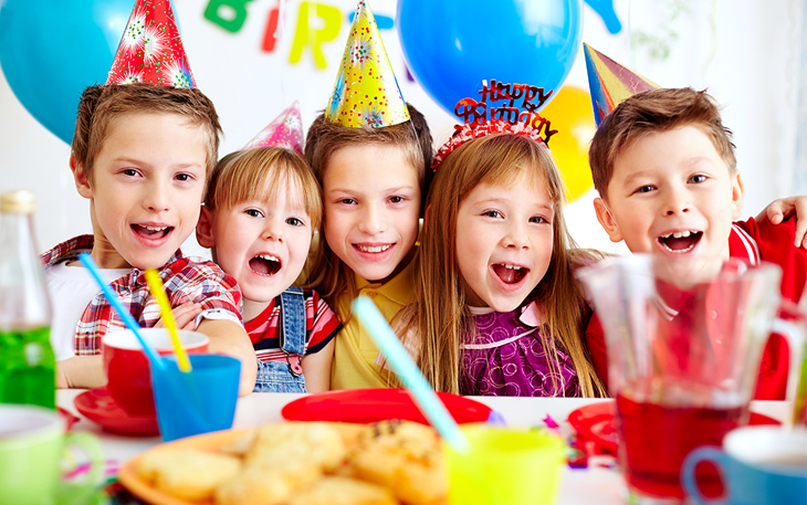 Kids take a group photo at a birthday party with balloons in the background