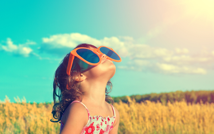 Little girl in wheat field wearing sunglasses and looking at the sun.