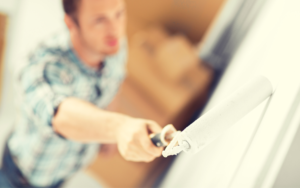 A man painting the wall white with a roller painter
