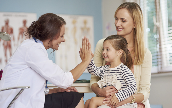 Mother holding her young daughter who is high-fiving her doctor.