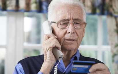 Elderly man on phone looking skeptically at his credit card