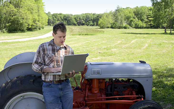 Man in front of a tractor using a laptop