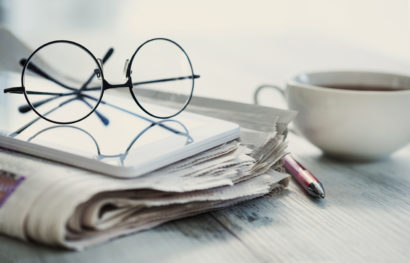 Stack of newspapers, eyeglasses on table