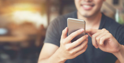 Young man sitting at a table looking at his cell phone in his hand