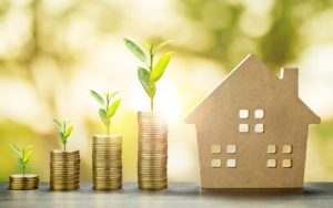 Four stacks of coins with plant growing and house to save for a mortgage