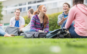 Group of six college students sitting in the grass laughing and talking in a group