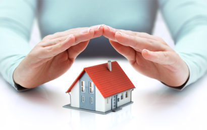 A pair of hands making a triangle above a small model house sitting on a table.