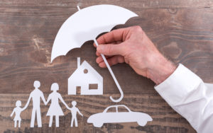 Man's hand holding a paper umbrella over a paper family, house and car.