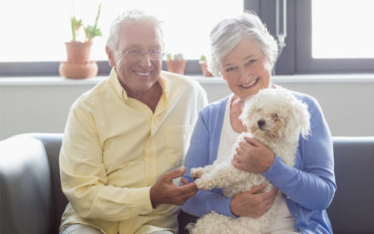 Senior couple sitting on a couch smiling. The woman is holding