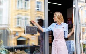 Woman puts an 'open' sign up on the window of her floral shop.