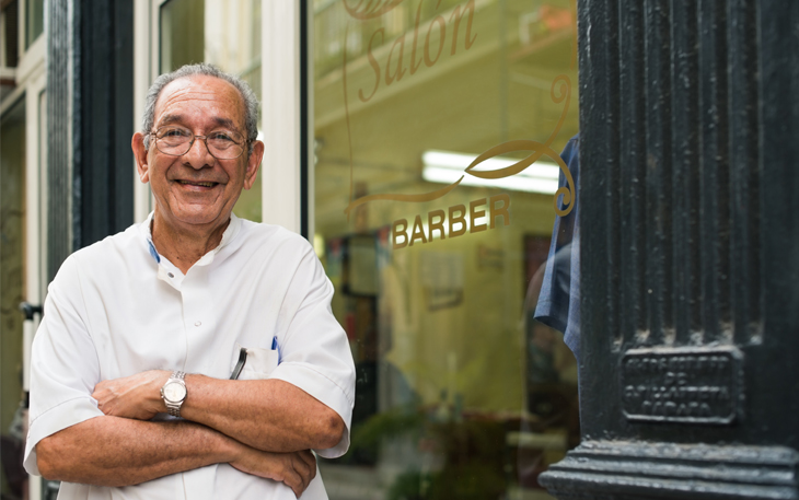 Man of retirement age stands outside of his barbershop business