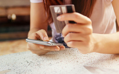 Woman holds a credit card and uses her phone