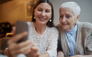 Adult daughter and elder mother smile while looking at a phone.