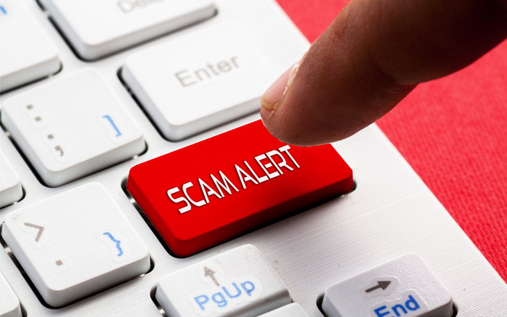 Finger hovers over the words "Scam Alert" on a keyboard.