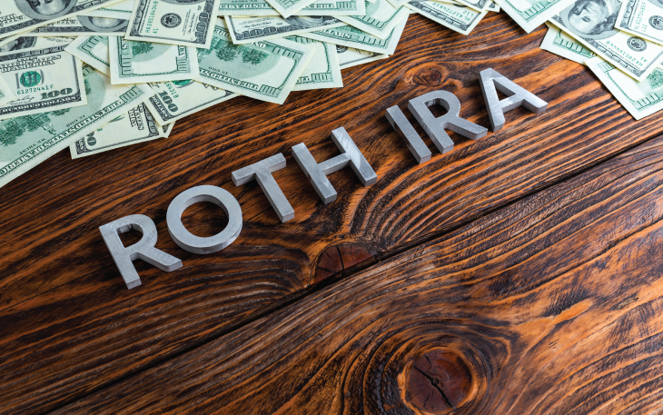 The words Roth IRA are on a desk with cash