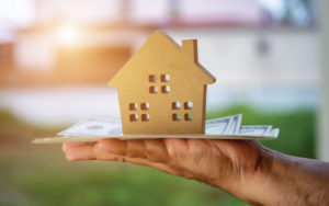 Cardboard home on top of a hand holding money.