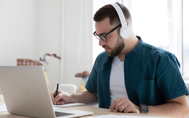 College Graduate working on his budget on his computer with headphones on