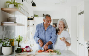 Retirement-aged man and woman in their kitchen cutting vegetables.